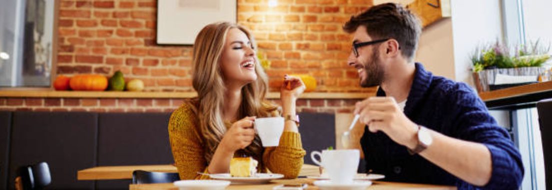 Blonde woman and brunette man on a coffee date looking at each other and laughing.